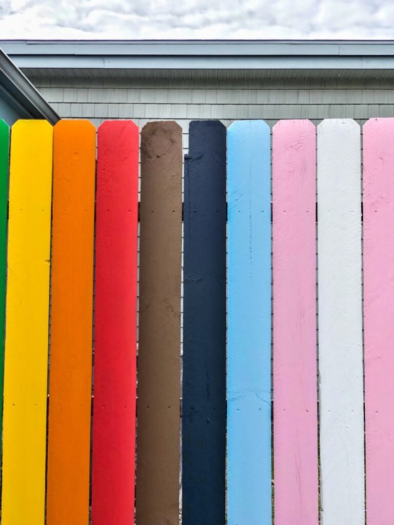 Colorful privacy picket fence surrounding house building home with tall painted wooden slats