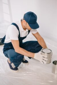 young painter in overalls and cap holding can with paint